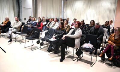 Fotografija prikazuje skupinu odraslih ljudi koji sjede u učionici ili dvorani za predavanja. Svi su okrenuti prema prednjem dijelu prostorije, kao da slušaju predavanje, prezentaciju ili radionicu.