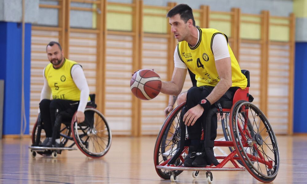 Fotografija prikazuje košarkaša u kolicima u žutom dresu kako vodi loptu.