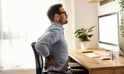 Muškarac sjedi za računalom i drži se za donji dio leđa zbog bolova.