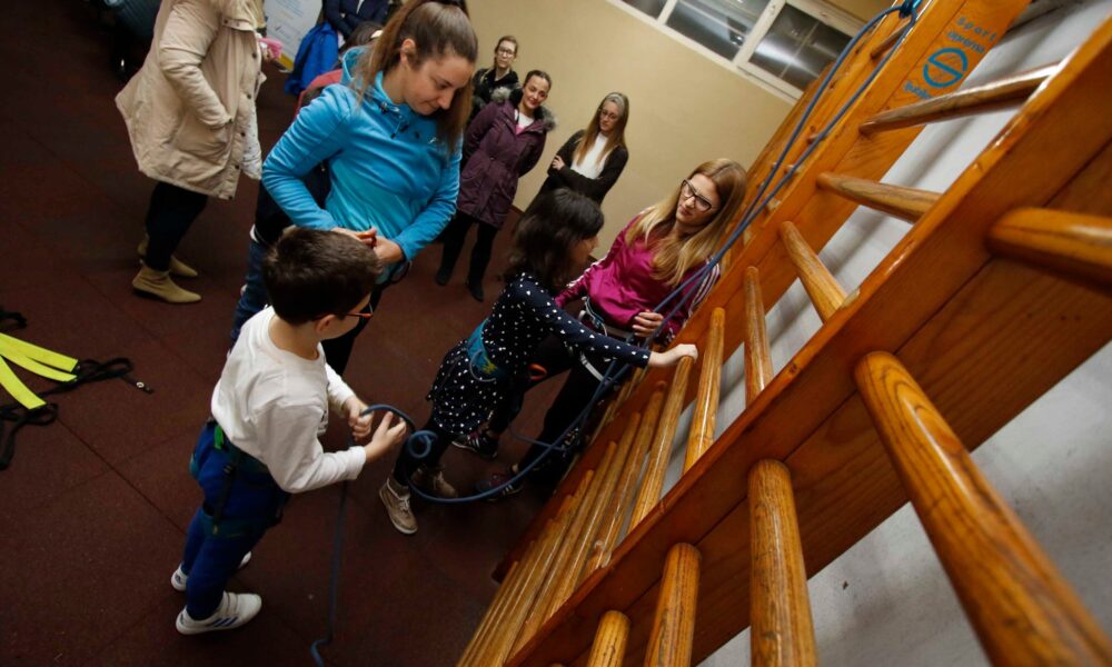 Slika prikazuje više djece kako rade fizičke aktivnosati, dok se neki žele popesti užetom na ljestve.