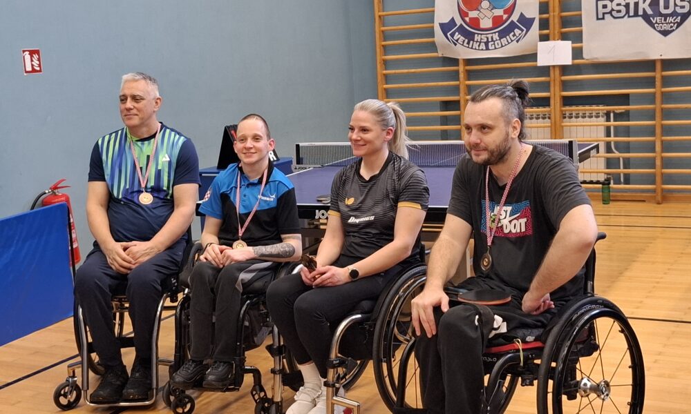Fotografija prikazuje četvero ljudi u invalidskim kolicima. Troje ih oko vrata ima medalje, a jedna u ruci drži nagradu.