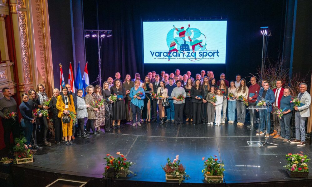 Fotografija prikazuje više ljudi svečano obučenih kako stoje na pozornici sa cvijećem i nagradama u ruci.