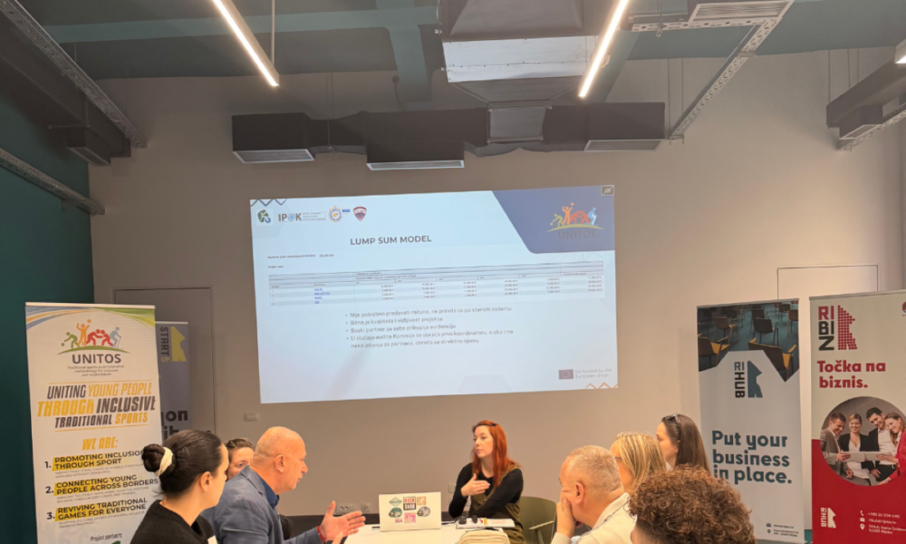 Na fotografiji je šest osoba koje sjede oko konferencijskog stola u modernoj, dobro osvijetljenoj dvorani za sastanke. Atmosfera djeluje profesionalno i usmjerena na zajednički rad, kao da sudionici sudjeluju u radionici, edukaciji ili projektnoj raspravi.