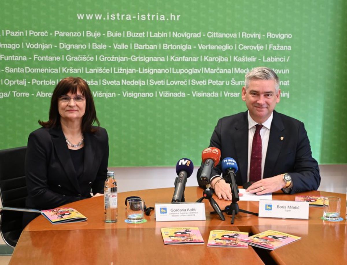 Na fotografiji su dvoje ljudi za konferencijskim stolom, ispred zelenog zida na kojem se vidi naziv službene stranice Istarske županije i popis istarskih gradova i općina.