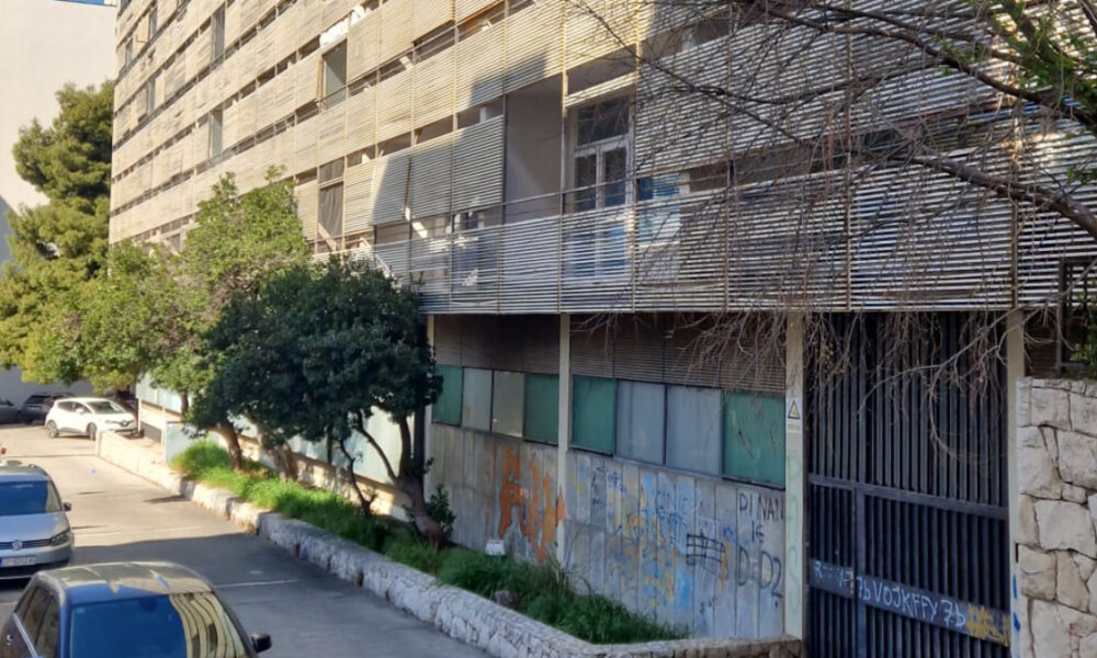 Ulaz i prizemlje Doma željezničara u Splitu s grafitima i parkiranim automobilima.