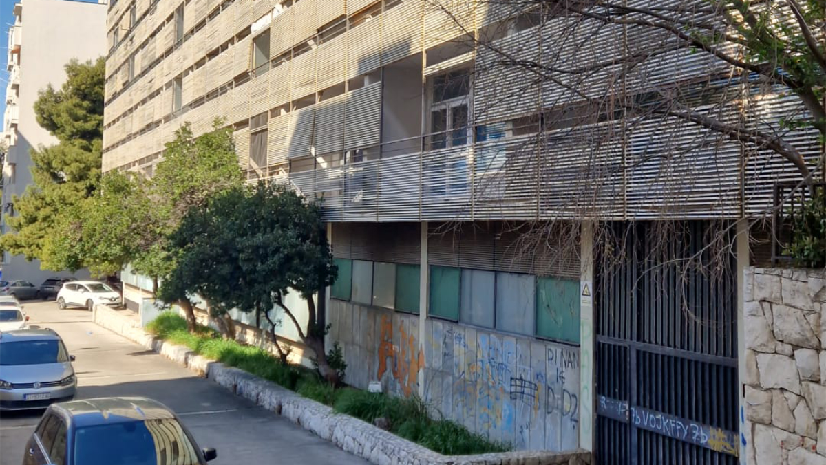 Ulaz i prizemlje Doma željezničara u Splitu s grafitima i parkiranim automobilima.