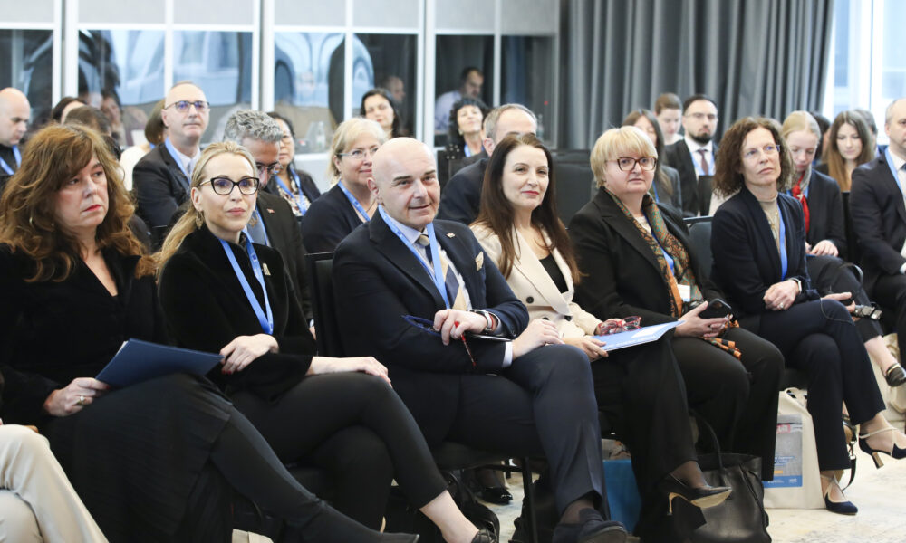 Publika na konferenciji sjedi i prati izlaganje u dvorani.