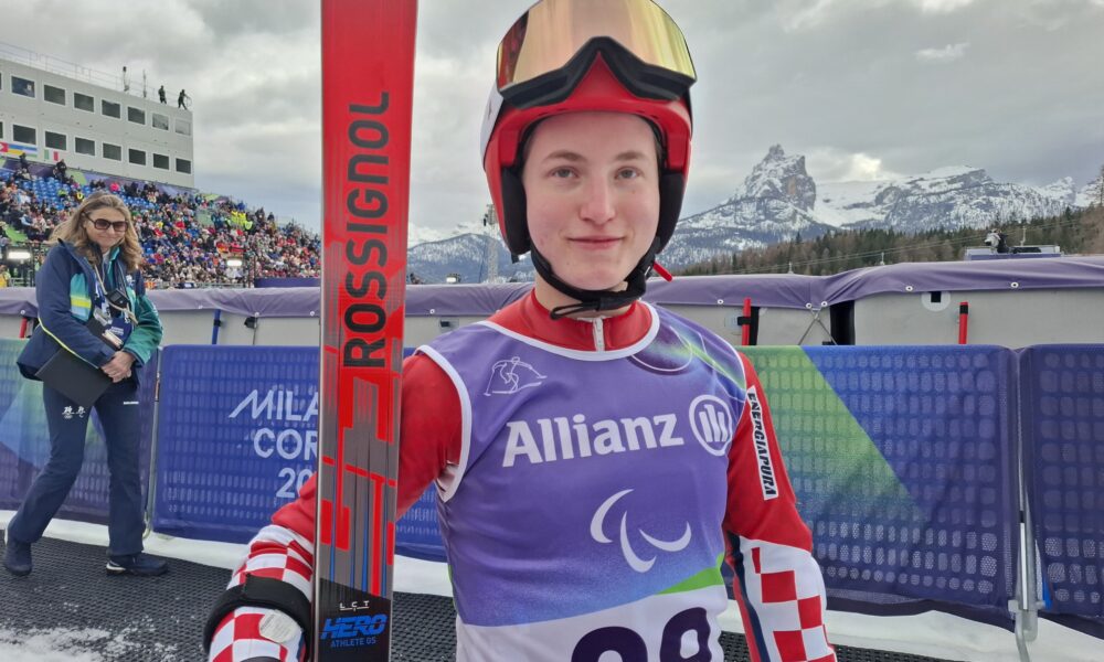 Fotografija prikazuje skijašicu u skijaškom odjelu i skijama u ruci.