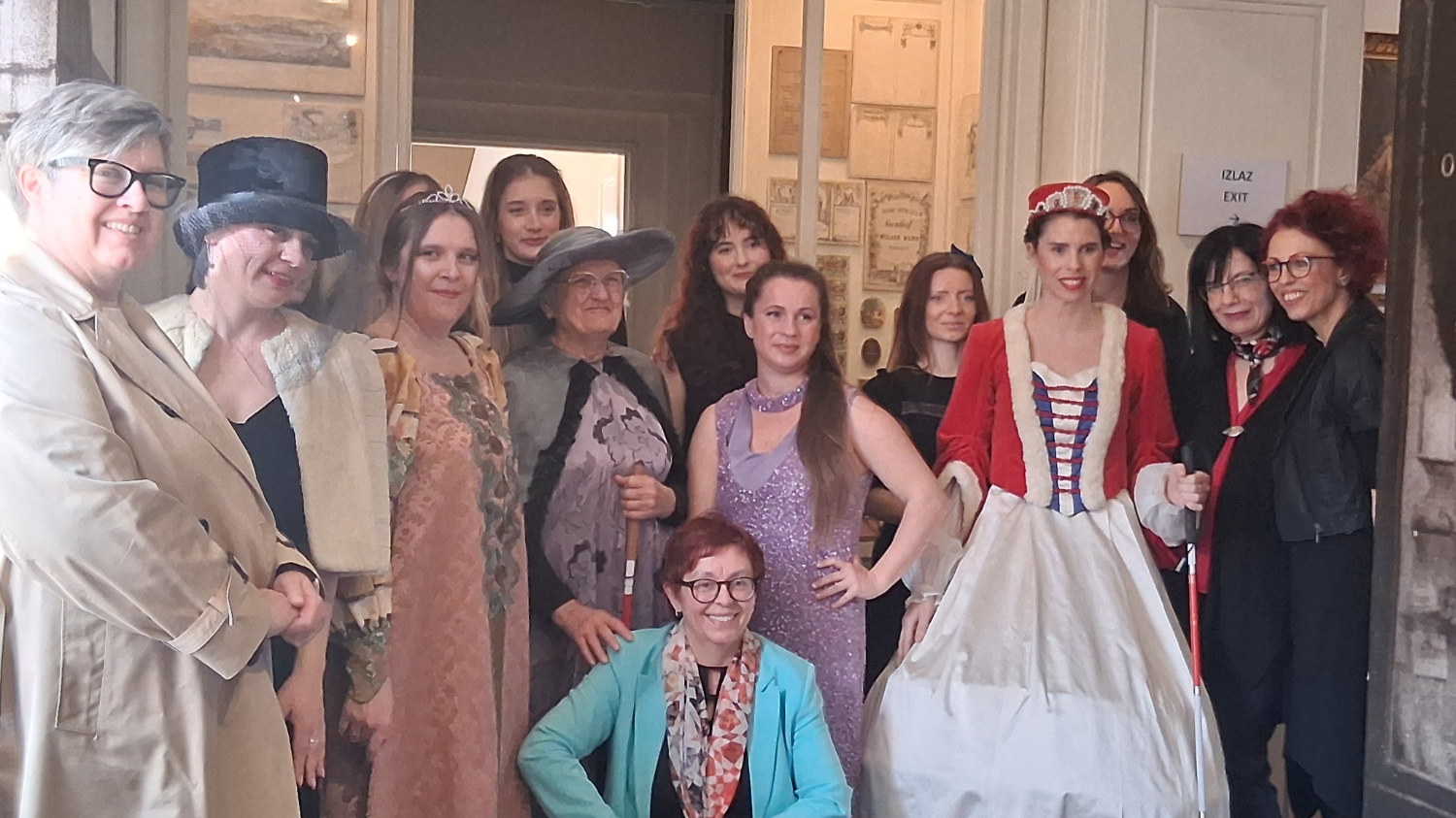 Sudionice i modeli u kostimima poziraju na kulturnom događanju u unutarnjem prostoru muzeja ili galerije.