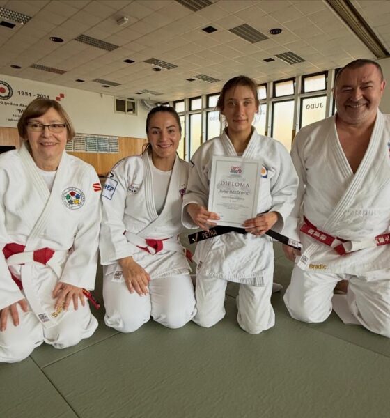 Fotografija prikazuje četvero ljudi obučenih u bijeli kimono kako kleče u dvorani. Jedna osoba u rukama drži diplomu. Ona ima crni pojas, a troje drugih ljudi crveni.