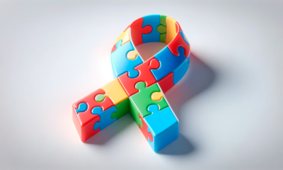 Na fotografiji je prikazana stilizirana vrpca u obliku petlje, sastavljena od šarenih dijelova slagalice (puzzle). Dominiraju jarke boje poput plave, crvene, zelene i žute, koje se međusobno isprepliću u obliku trodimenzionalne vrpce. Oblik podsjeća na simbol podrške i svijesti, a motiv puzzli često se povezuje s autizmom, simbolizirajući raznolikost, kompleksnost i jedinstvenost osoba iz spektra autizma. Vrpca je postavljena na svijetloj, neutralnoj podlozi, što dodatno naglašava njezine boje i oblik.