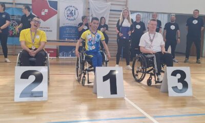 Fotografija prikazuje tri sportaša u kolicima s medaljama oko vrata, dok je ispred njih redni broj mjesta kojeg su osvojili.