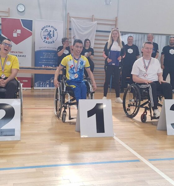 Fotografija prikazuje tri sportaša u kolicima s medaljama oko vrata, dok je ispred njih redni broj mjesta kojeg su osvojili.