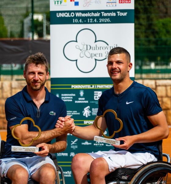 Fotograafija prikazuje dvoje ljudi u kolicima koji drže nagrade u jednoj, a pozdravljaju se s drugom rukom. Oni se nalaze na zemljanoj površini nekog teniskog terena.