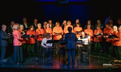 Fotografija prikazuje zbor pjevača i dirigenta kako nastupaju