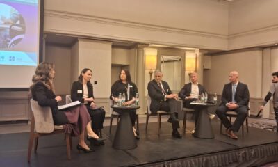 Fotografija prikazuje nekoliko ljudi kako sjedi za stolom i priča, a iza njih se nalazi video zid.