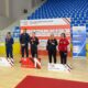Fotografijha prikazuje nekoliko ljudi u paru po dvoje kako stoje na postolju s medaljamaoko vrata.