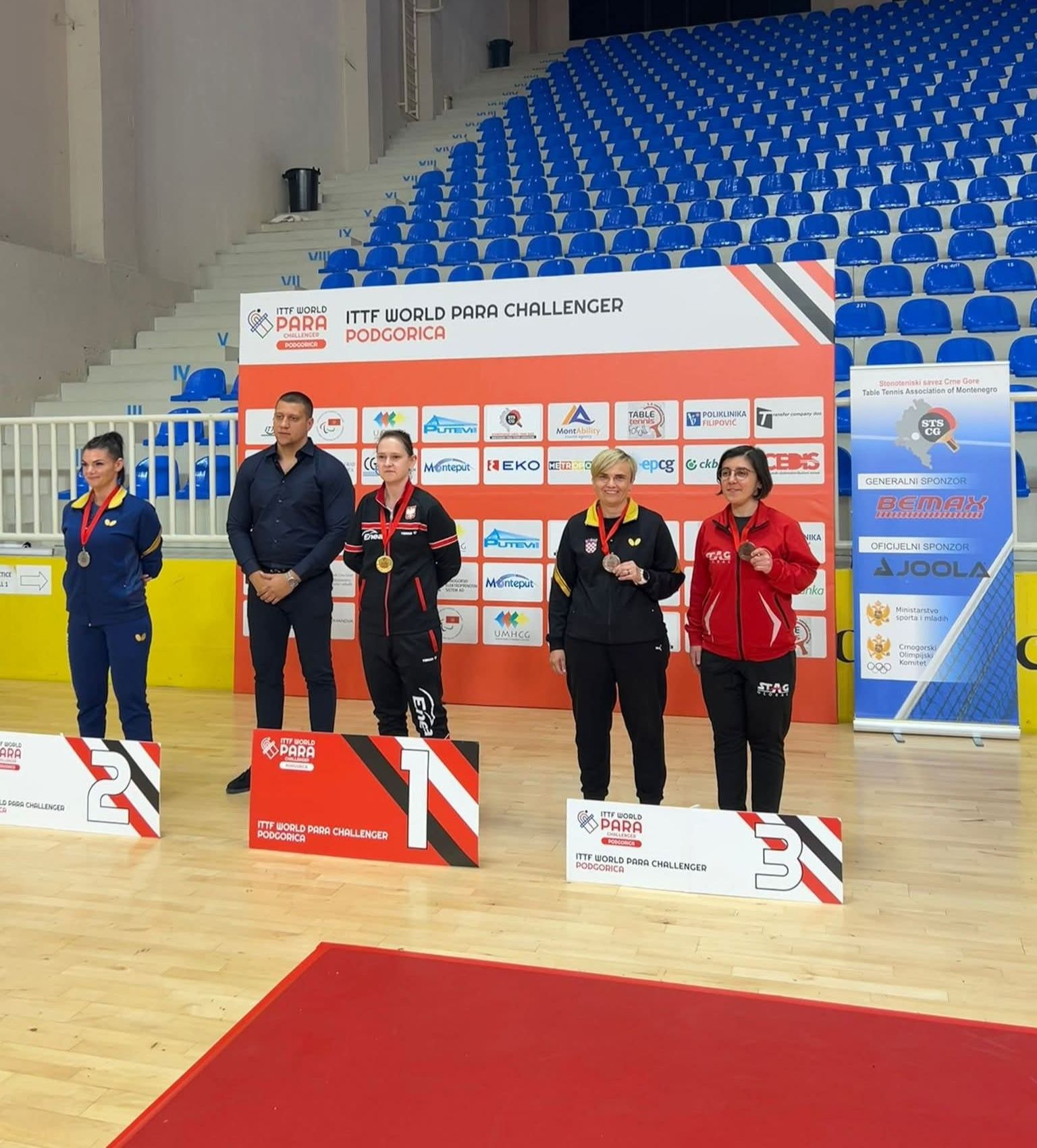 Fotografijha prikazuje nekoliko ljudi u paru po dvoje kako stoje na postolju s medaljamaoko vrata.