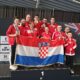 Fotografija prikazuje nekoliko ljudi u crvenim trenirkama s medaljama oko vrata kako drže Hrvatsku zastavu.