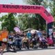 Na fotografiji je prikazan početak humanitarne utrke „Run for MD“ na otvorenom, uz velik broj sudionika različite dobi. Trkači i osobe u invalidskim kolicima zajedno kreću ispod velikog ružičasto-crnog startnog luka s natpisom „keindl-sport.hr“. Događaj se odvija po sunčanom danu u prirodnom okruženju, a uz stazu su okupljeni gledatelji i volonteri. Fotografija prenosi atmosferu zajedništva, inkluzije i podrške osobama s mišićnom distrofijom i drugim neuromuskularnim bolestima.