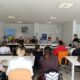 Na fotografiji je prikazan skup i radionica održana u svijetloj konferencijskoj prostoriji. Sudionici sjede za stolovima raspoređenima u obliku slova U te pažljivo slušaju govornicu koja stoji s desne strane prostorije i obraća se okupljenima. U prvom planu vide se sudionici okrenuti prema panelu predavača, među kojima su i osobe koje koriste invalidska kolica. Za glavnim stolom sjedi nekoliko sudionika i predstavnika organizacija, a iza njih se nalazi roll-up plakat SOIH-a i promotivni materijali povezani s pravima osoba s invaliditetom i neovisnim življenjem. Atmosfera djeluje radno, ali ugodno i uključivo, s naglaskom na razgovor, suradnju i razmjenu iskustava među sudionicima.