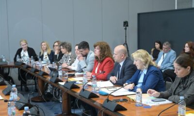 Na fotografiji je prikazan sastanak za dugim konferencijskim stolom, vjerojatno u službenom ili institucionalnom prostoru poput saborske dvorane ili prostorije za sjednice. Za stolom sjedi veći broj sudionika, među kojima su žene i muškarci, odjeveni uglavnom poslovno, što upućuje na formalni karakter događaja. Sudionici imaju ispred sebe mikrofone, dokumente, bilježnice i boce vode, a neki zapisuju bilješke ili pažljivo slušaju govornike. Atmosfera djeluje ozbiljno i koncentrirano, kao tijekom rasprave ili tematske sjednice. U pozadini se vidi kamera na stativu, što sugerira da se događaj snima ili dokumentira. Cjelokupni dojam fotografije upućuje na službenu raspravu ili sastanak stručnjaka i predstavnika institucija.