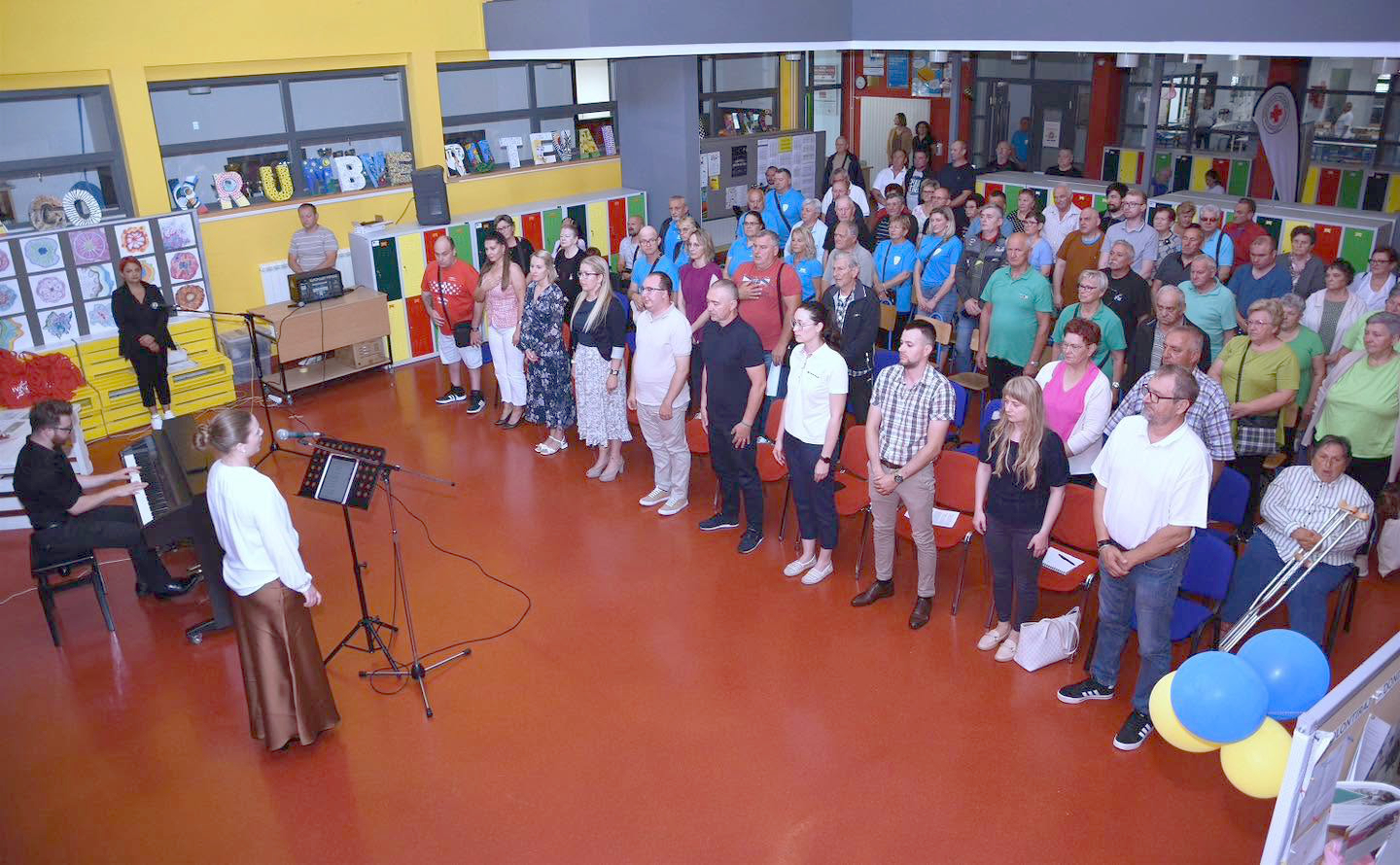 Sudionici stoje tijekom svečanosti u školskom atriju uz glazbeni nastup.