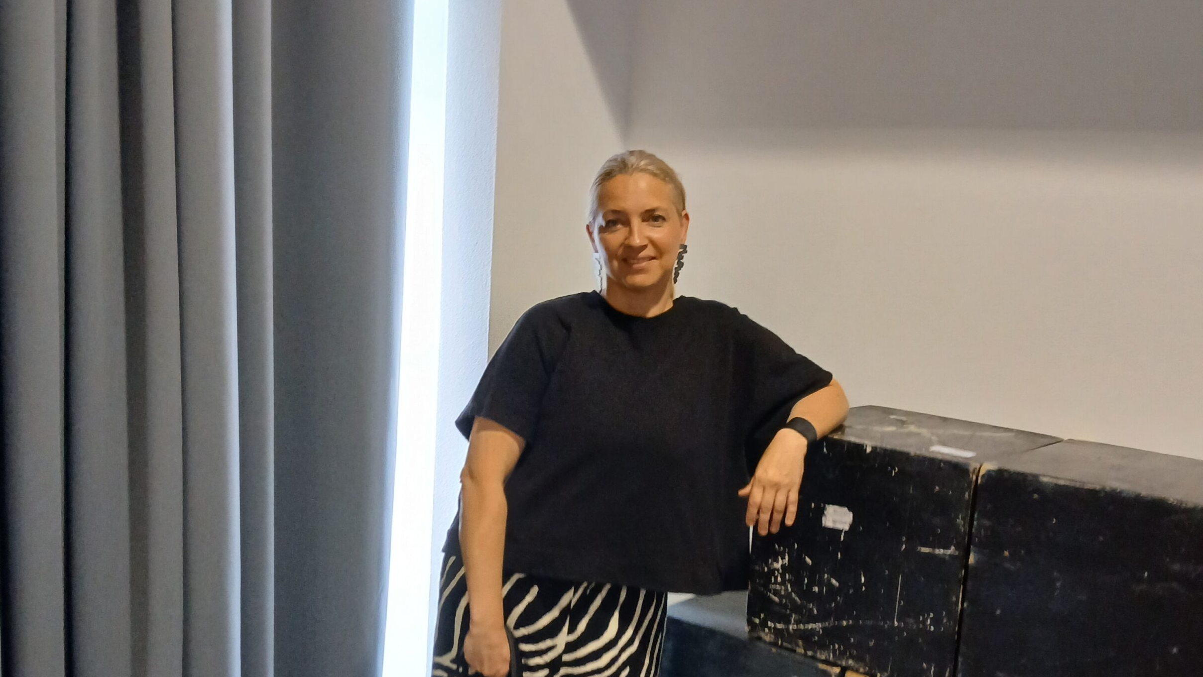 Žena stoji uz kutije u unutarnjem prostoru i gleda prema kameri.