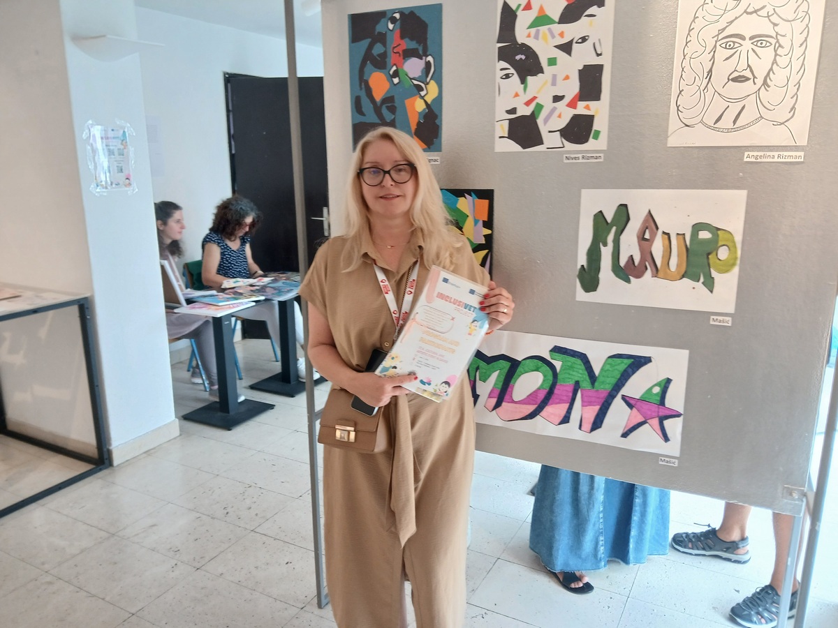 Žena drži priznanje pokraj izloženih likovnih radova na izložbi.