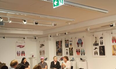 a fotografiji je prikazan razgovor nakon projekcije dokumentarnog filma u izložbenom prostoru kulturnog centra. U prvom planu nalazi se publika koja pažljivo prati panel-raspravu, dok na pozornici sjede četiri sudionika događanja. Jedna od govornica drži mikrofon i obraća se okupljenima, dok ostali sudionici pozorno slušaju. Prostor je uređen kao galerija, a zidove krase izložbeni panoi s fotografijama i umjetničkim prikazima obuće, što dodatno doprinosi umjetničkom ozračju događanja. Atmosfera djeluje ugodno, otvoreno i poticajno za razmjenu ideja, a velik odaziv publike svjedoči o interesu za teme inkluzivne umjetnosti i kulturne suradnje.