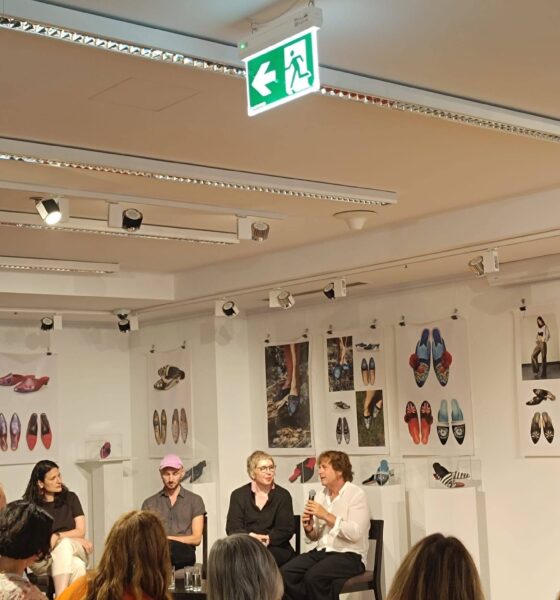 a fotografiji je prikazan razgovor nakon projekcije dokumentarnog filma u izložbenom prostoru kulturnog centra. U prvom planu nalazi se publika koja pažljivo prati panel-raspravu, dok na pozornici sjede četiri sudionika događanja. Jedna od govornica drži mikrofon i obraća se okupljenima, dok ostali sudionici pozorno slušaju. Prostor je uređen kao galerija, a zidove krase izložbeni panoi s fotografijama i umjetničkim prikazima obuće, što dodatno doprinosi umjetničkom ozračju događanja. Atmosfera djeluje ugodno, otvoreno i poticajno za razmjenu ideja, a velik odaziv publike svjedoči o interesu za teme inkluzivne umjetnosti i kulturne suradnje.