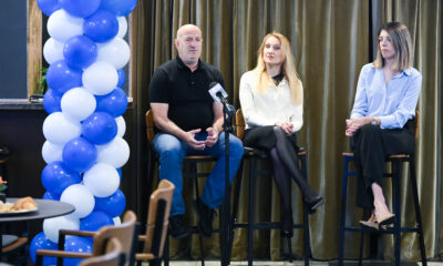 Panel-rasprava s troje sudionika ispred mikrofona i plavo-bijele dekoracije od balona.