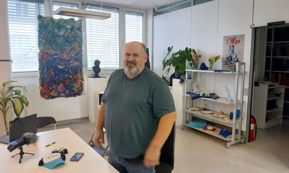 Muškarac stoji u uredu ispred stola za razgovor, okružen umjetničkim radovima i biljkama.