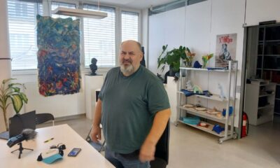 Muškarac stoji u uredu ispred stola za razgovor, okružen umjetničkim radovima i biljkama.