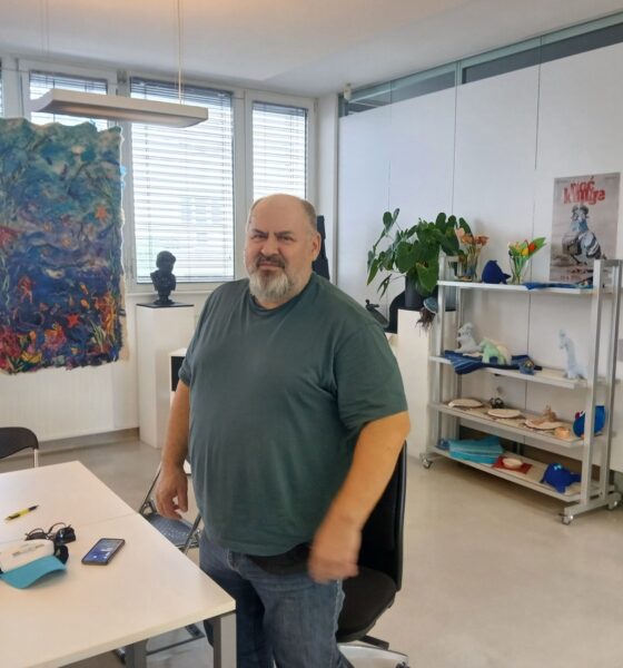 Muškarac stoji u uredu ispred stola za razgovor, okružen umjetničkim radovima i biljkama.