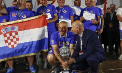 Na fotografiji je prikazan svečani trenutak dodjele pehara hrvatskoj reprezentaciji osoba s invaliditetom nakon osvajanja naslova viceprvaka svijeta u sportskom ribolovu. U prvom planu nekoliko članova reprezentacije, odjevenih u plave sportske majice s hrvatskim grbom, ponosno drže veliki srebrni pehar i hrvatsku zastavu. Natjecatelji oko vrata imaju medalje, a neki u rukama drže diplome i priznanja. Atmosfera je svečana i emotivna, a osmijesi i slavlje članova ekipe pokazuju zadovoljstvo velikim sportskim uspjehom. U pozadini se vide ostali sudionici i uzvanici na pozornici tijekom završne ceremonije prvenstva u Ivancu.