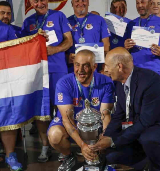 Na fotografiji je prikazan svečani trenutak dodjele pehara hrvatskoj reprezentaciji osoba s invaliditetom nakon osvajanja naslova viceprvaka svijeta u sportskom ribolovu. U prvom planu nekoliko članova reprezentacije, odjevenih u plave sportske majice s hrvatskim grbom, ponosno drže veliki srebrni pehar i hrvatsku zastavu. Natjecatelji oko vrata imaju medalje, a neki u rukama drže diplome i priznanja. Atmosfera je svečana i emotivna, a osmijesi i slavlje članova ekipe pokazuju zadovoljstvo velikim sportskim uspjehom. U pozadini se vide ostali sudionici i uzvanici na pozornici tijekom završne ceremonije prvenstva u Ivancu.