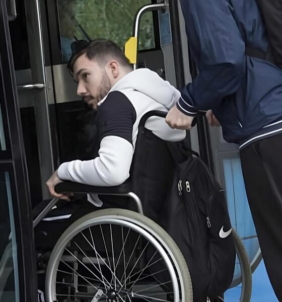 Na fotografiji se vidi osoba u invalidskim kolicima kojoj druga osoba pomaže pri ulasku u niskopodni autobus. Osoba u kolicima nalazi se na ulazu u vozilo i jednom rukom pridržava okvir vrata, dok je iza nje osoba koja gura kolica i pomaže pri ukrcaju. Fotografija naglašava važnost pristupačnog javnog prijevoza i uloge osobne asistencije u omogućavanju samostalnijeg kretanja osoba s invaliditetom. Prikazuje svakodnevnu situaciju u kojoj prilagođena vozila i podrška druge osobe omogućuju lakše korištenje javnog prijevoza.