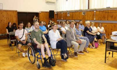 Na fotografiji je prikazan skup povodom obilježavanja obljetnice Centra za pružanje usluga u zajednici Varaždin. U prvom planu sjede uzvanici i korisnici Centra, među kojima je i osoba u invalidskim kolicima, što dodatno naglašava inkluzivni karakter događanja. Sudionici pažljivo prate program koji se odvija u dvorani. Prostorija je ispunjena brojnim posjetiteljima, a u pozadini se mogu vidjeti redovi sjedećih mjesta i osoba koja fotografira događaj. Topla i svečana atmosfera odražava zajedništvo, podršku i važnost rada Centra za lokalnu zajednicu.