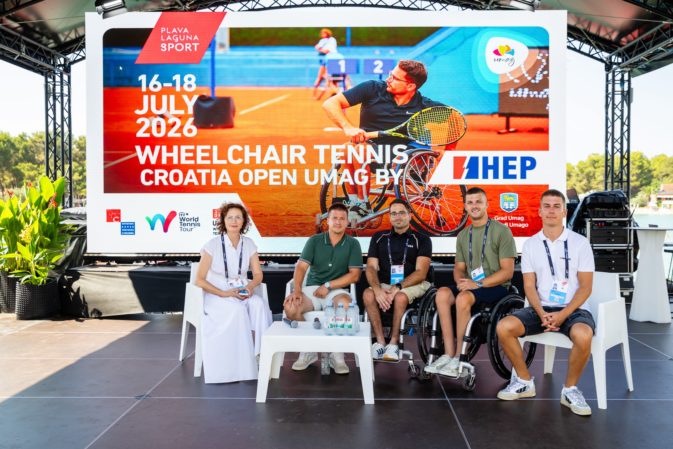 Na fotografiji se nalazi pet osoba koje sjede na pozornici ispred velikog promotivnog ekrana za Wheelchair Tennis Croatia Open Umag by HEP, koji se održava od 16. do 18. srpnja 2026. u Umagu. U pozadini dominira veliki plakat s fotografijom tenisača u kolicima tijekom igre te logotipi organizatora i partnera turnira. Za stolom ispred sudionika nalaze se boce vode i mikrofon, što upućuje na to da je riječ o službenom predstavljanju ili ždrijebu turnira. Među okupljenima su predstavnici organizatora i hrvatski tenisači u kolicima koji će nastupiti na turniru. Fotografija odiše sportskom i svečanom atmosferom te najavljuje početak još jednog izdanja međunarodnog turnira tenisa u kolicima u Umagu.
