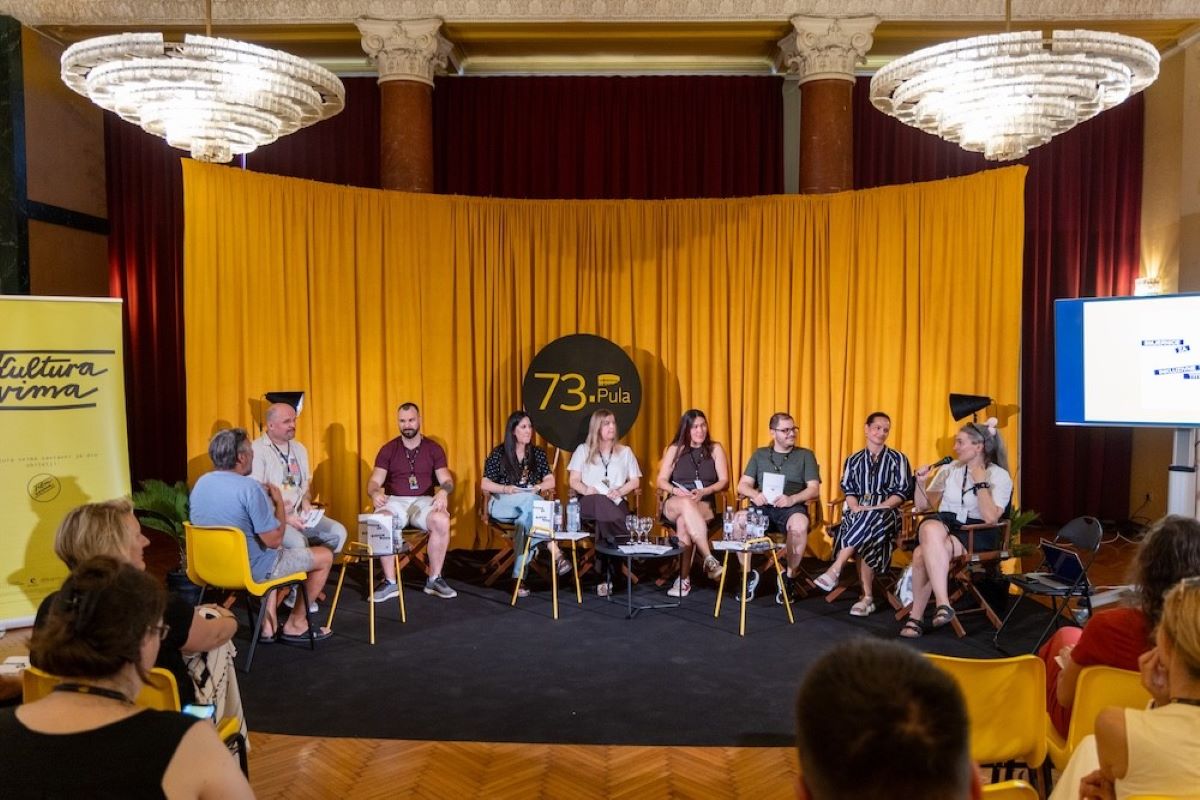 Na fotografiji je prikazano predstavljanje Smjernica svima svugdje održano u sklopu programa Pula PRO na 73. Pula Film Festivalu. Na pozornici ispred prepoznatljive žute festivalske scenografije sjedi sedmero sudionika panel-razgovora, dok jedna govornica drži mikrofon i obraća se publici. Uz sudionike su postavljeni stolovi s primjercima Smjernica i osvježenjem, a iza njih istaknut je znak 73. Pula Film Festivala. S lijeve strane nalazi se banner organizacije Kultura svima, dok je s desne strane ekran s prezentacijom. U prvom planu vidi se publika koja prati predstavljanje u Crvenom salonu Doma hrvatskih branitelja.