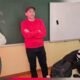 Na fotografiji se nalaze tri osobe u učionici ili informatičkom kabinetu. U središtu fotografije stoji muškarac u crvenoj majici i tamnoj kapi, prekriženih ruku, dok govori ili se obraća prisutnima. S njegove lijeve strane stoji žena u svijetlom džemperu i trapericama, također prekriženih ruku, koja pažljivo prati događanja. S desne strane sjedi žena za računalom i radi na računalu. U pozadini se vidi školska ploča s ispisanim matematičkim formulama i bijela projekcijska ploča, što upućuje na to da je fotografija snimljena tijekom predavanja, radionice ili edukativne aktivnosti u školi. Atmosfera djeluje radno i edukativno, a sudionici su usmjereni na zajedničku aktivnost ili prezentaciju.