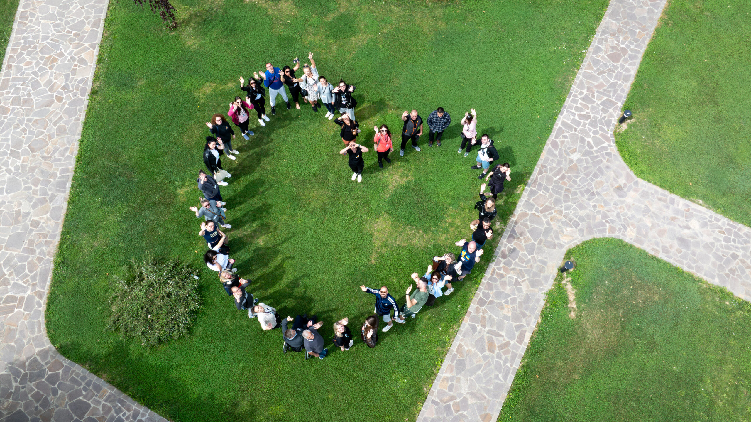 Na fotografiji snimljenoj iz zraka skupina ljudi stoji na zelenoj travnatoj površini i svojim rasporedom tvori veliki simbol MS Heart, međunarodni znak zajedništva i solidarnosti s osobama koje žive s multiplom sklerozom. Sudionici gledaju prema kameri, mašu i osmjehuju se, stvarajući dojam zajedništva, pozitivne energije i međusobne podrške. Simbol je okružen kamenim pješačkim stazama koje dodatno ističu njegov oblik, dok zelena površina naglašava kontrast i čini kompoziciju preglednom. Fotografija je nastala tijekom 4. Networking Meeta mladih s MS-om, a prikazuje mlade osobe koje svojim sudjelovanjem šalju snažnu poruku povezanosti, uključivosti i zajedničke borbe za bolji položaj osoba koje žive s multiplom sklerozom. Ova fotografija osvojila je međunarodno priznanje World MS Day Certificate of Appreciation u sklopu globalne kampanje World MS Day – MS Heart Challenge, kao simbol podrške, zajedništva i podizanja svijesti o multiploj sklerozi.