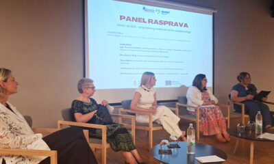 Sudionice panel rasprave sjede na pozornici ispred projekcije s naslovom „Odmor od skrbi – od projektnog modela do održive socijalne usluge”. Rasprava je posvećena razvoju usluge predaha za njegovatelje, a ispred sudionica nalaze se stolovi s vodom i čašama.