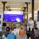 Na fotografiji je prikazan dio početne konferencije projekta „Podrška za snagu“, koju organizira Udruga osoba s mišićnom distrofijom Primorsko-goranske županije. U prvom planu nalazi se publika koja prati predstavljanje projekta, dok su na pozornici tri sudionika panela. Jedan od govornika koristi elektromotorna invalidska kolica, čime fotografija dodatno naglašava uključivost i usmjerenost projekta na osobe s invaliditetom. U pozadini se nalazi veliki ekran s naslovom projekta „Podrška za snagu“ i oznakom početne konferencije, uz logotipe organizatora i Europskog socijalnog fonda plus. S lijeve i desne strane postavljeni su promotivni roll-up banneri Udruge i projekta s informacijama o ciljevima, aktivnostima i financijskoj potpori. Konferencija se održava u modernom, prostranom prostoru Gradske knjižnice Rijeka, što doprinosi profesionalnom i otvorenom ozračju događanja. Fotografija prikazuje atmosferu predstavljanja projekta te naglašava važnost razvoja socijalnih usluga, pristupačnosti i uključivanja osoba s invaliditetom u život zajednice.