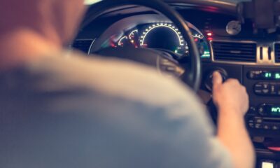 Na fotografiji se vidi unutrašnjost automobila iz perspektive stražnjeg sjedala. U prvom planu nalazi se vozač, čije su lice i tijelo zamućeni, dok desnom rukom poseže prema kontakt-bravi, vjerojatno kako bi upalio ili ugasio vozilo. U pozadini se jasno vide upravljač, osvijetljena instrumentna ploča s brzinomjerom i kontrolna ploča automobila. Na vjetrobranskom staklu postavljen je držač za mobitel, što sugerira da je riječ o taksi-vozilu ili automobilu koji se koristi za navigaciju. Fotografija stvara dojam svakodnevne vožnje i fokusira se na trenutak kada vozač upravlja ili priprema vozilo za polazak.