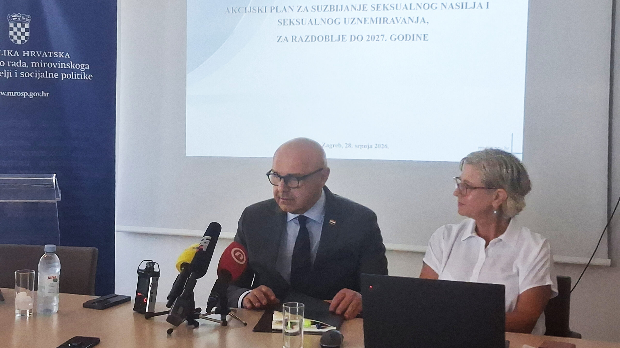 Na konferenciji za medije predstavljen je Akcijski plan za suzbijanje seksualnog nasilja i seksualnog uznemiravanja do 2027. godine. Za stolom sjede dvije osobe, ispred njih su mikrofoni i prijenosno računalo, dok je u pozadini projiciran naslov dokumenta i datum predstavljanja.
