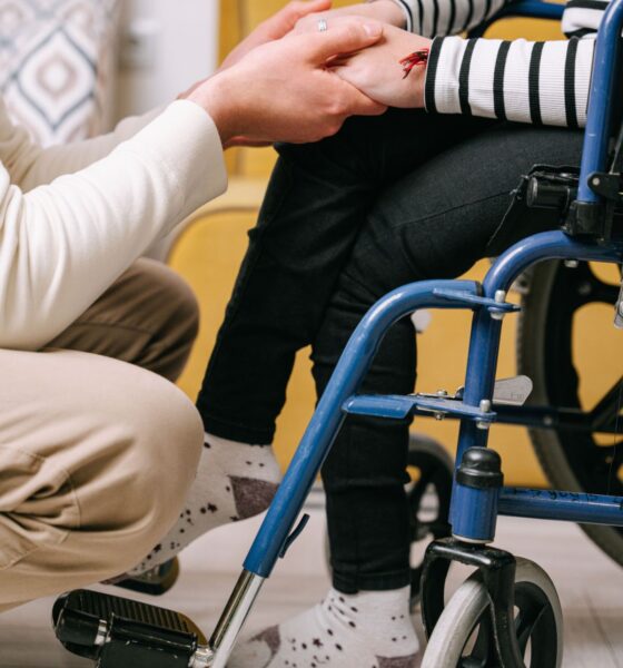 Osoba pruža podršku osobi u invalidskim kolicima držeći je za ruku.