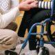 Osoba pruža podršku osobi u invalidskim kolicima držeći je za ruku.
