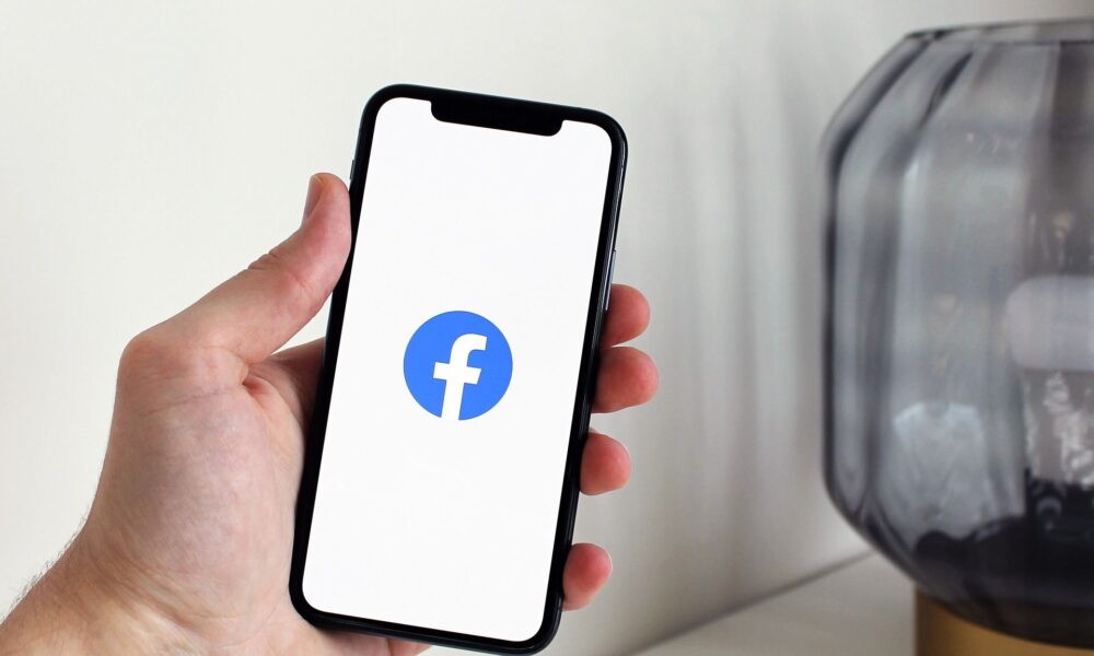 Ruka drži pametni telefon na čijem je zaslonu prikazan logotip Facebooka.